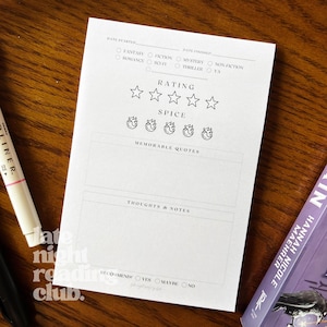 May include: A white book with a black and white book review tracker. The tracker includes sections for date started, date finished, genre, rating, spice level, memorable quotes, thoughts and notes, and a recommendation section.