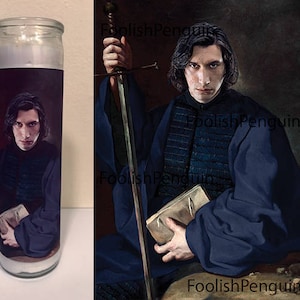 May include: A white candle with a dark image of a man holding a book and a sword. The man has dark hair and is wearing a dark blue robe. The candle is in a glass jar with a white label.