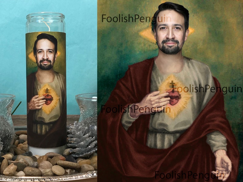 May include: A white candle with a printed image of a man with a beard and a heart with a cross on it. The image is surrounded by a yellow halo. The candle is on a silver tray with small rocks and a pine cone.