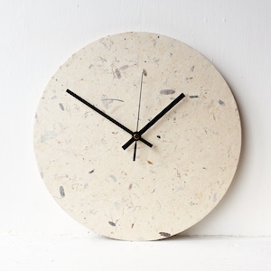 May include: A round, off-white wall clock with black hands and a textured, speckled surface.
