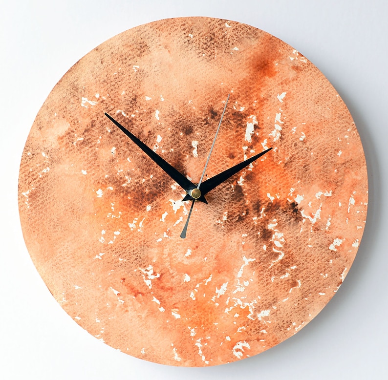 Puede incluir: Un reloj redondo de acuarela naranja y marr&oacute;n con manecillas negras.