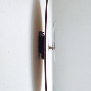 Puede incluir: Un reloj redondo de madera con agujas negras montado en una pared blanca.