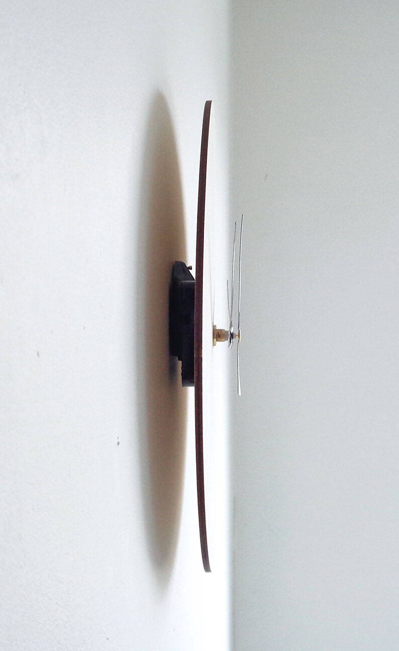 Puede incluir: Un reloj redondo de madera con agujas negras montado en una pared blanca.