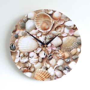 May include: A round clock featuring a seashell design. The clock face is covered in a variety of seashells, including clams, scallops, and conch shells. The clock hands are black and the clock face is white.
