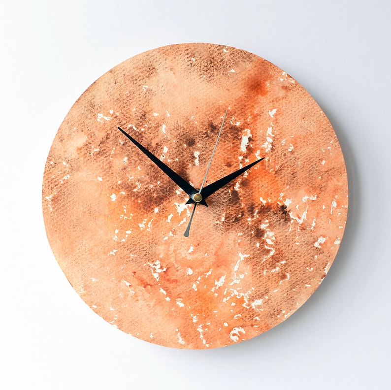 Puede incluir: Un reloj redondo de acuarela naranja y marr&oacute;n con manecillas negras.