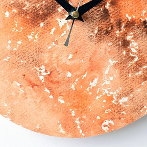 Puede incluir: Una esfera de reloj redonda con un dise&ntilde;o de acuarela en tonos naranja y marr&oacute;n. Las manecillas del reloj son negras.
