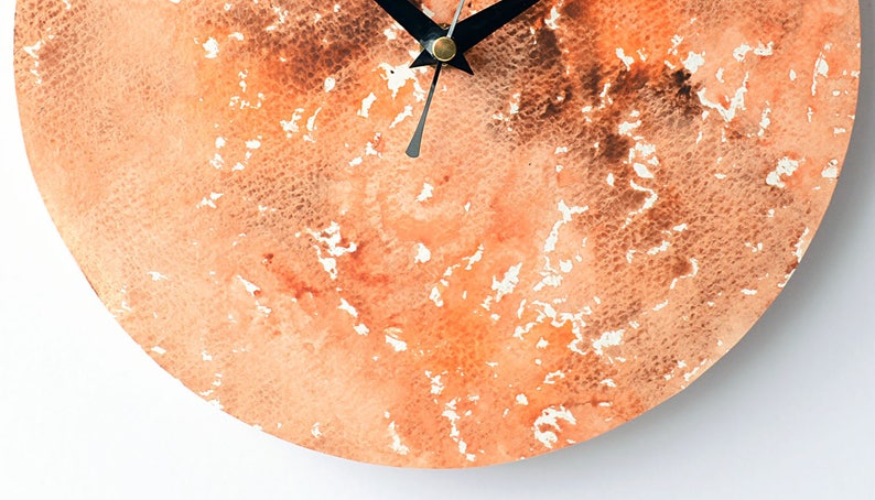 Puede incluir: Una esfera de reloj redonda con un dise&ntilde;o de acuarela en tonos naranja y marr&oacute;n. Las manecillas del reloj son negras.