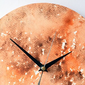 Puede incluir: Un reloj redondo con agujas negras sobre un fondo de acuarela. El fondo es una mezcla de naranja, marr&oacute;n y blanco.