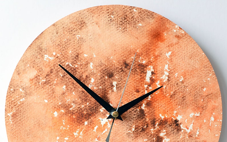 Puede incluir: Un reloj redondo con agujas negras sobre un fondo de acuarela. El fondo es una mezcla de naranja, marr&oacute;n y blanco.