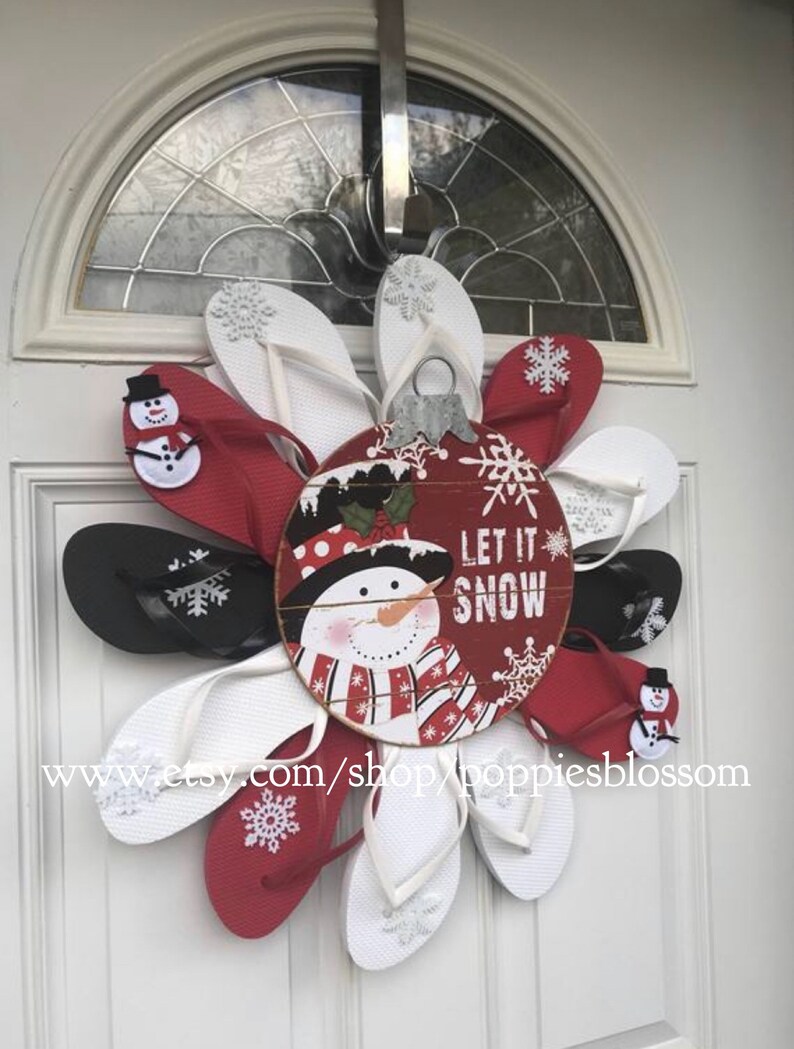 May include: A festive Christmas wreath made of red, white, and black flip-flops arranged in a circular pattern. A central ornament features a snowman and the words "Let it Snow".