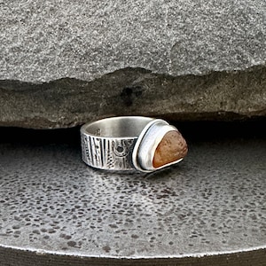 May include: A silver ring with a textured band and a brown agate stone set in a bezel.