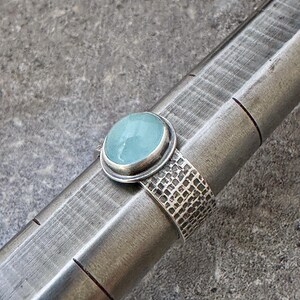 May include: A silver ring with a light blue gemstone set in a bezel setting. The band of the ring is textured with a hammered finish.