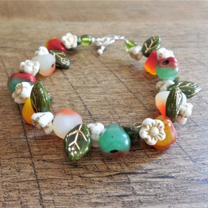 May include: A colourful bracelet featuring green leaves, white flowers, and red, orange, and green glass beads.