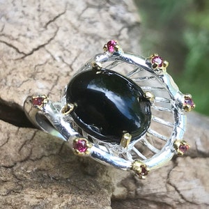 Peut inclure: Une bague en argent avec une pierre pr&eacute;cieuse noire entour&eacute;e de petites pierres pr&eacute;cieuses roses.