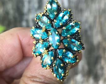 May include: A turquoise blue ring with a large, geometric design. The ring is made of silver and has a black oxidized finish. The ring is set with many small, faceted stones.