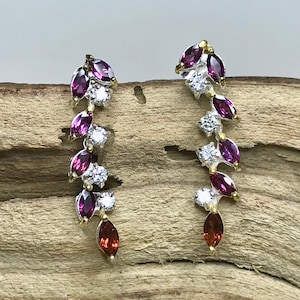 Puede incluir: Un par de pendientes de plata con un dise&ntilde;o en cascada de piedras de forma marquesa de color morado y rojo y piedras redondas transparentes.