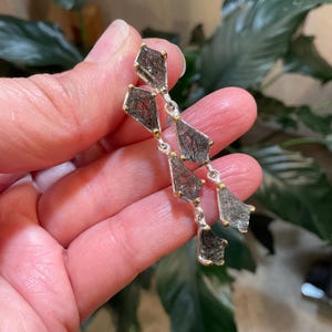 K&ouml;nnte beinhalten: Silberne Ohrringe mit einem baumelnden Design mit mehreren facettierten schwarzen Steinen mit goldenen Akzenten.