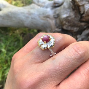 May include: A silver ring with a gold flower design and a pink gemstone in the center.