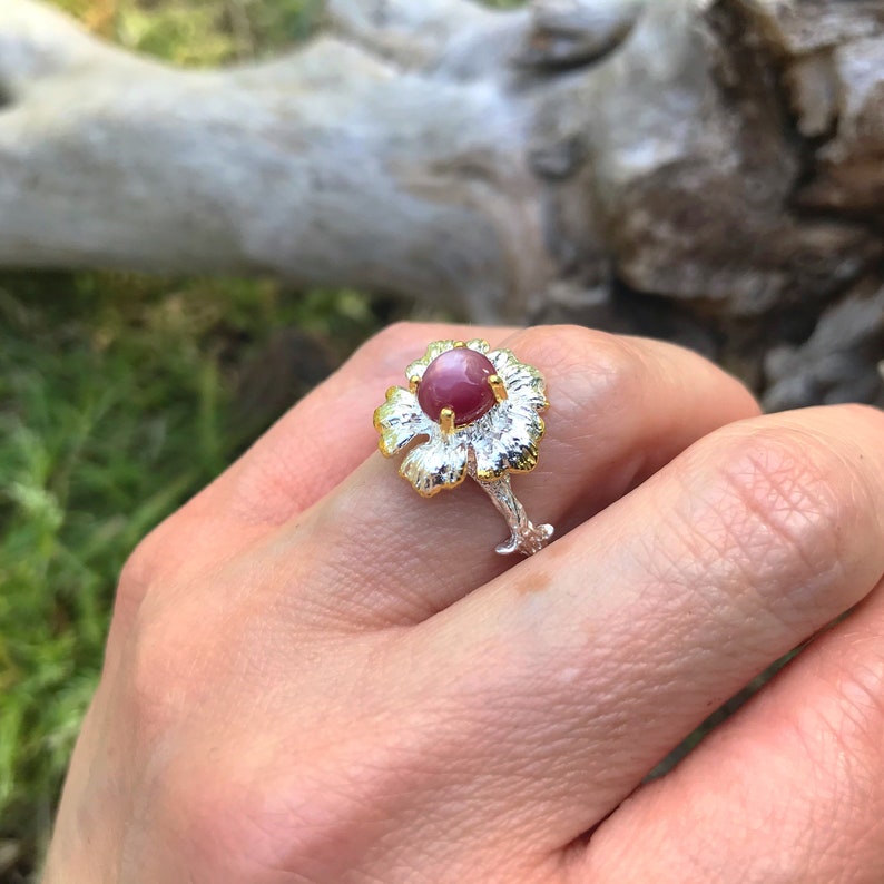 May include: A silver ring with a gold flower design and a pink gemstone in the center.
