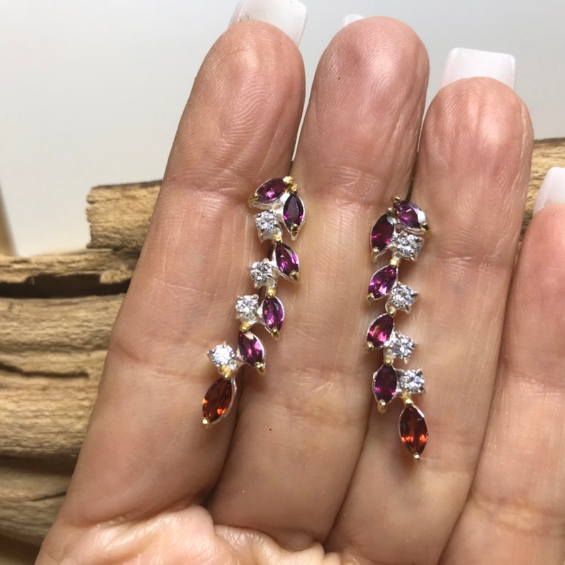 Puede incluir: Un par de pendientes colgantes con acabado plateado y dorado. Los pendientes presentan una cascada de peque&ntilde;as piedras preciosas de color p&uacute;rpura y rojo en forma de marquesa, acentuadas por piedras de circonita c&uacute;bica transparentes.