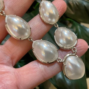 May include: A silver necklace with large, white, pearlescent, oval-shaped beads.