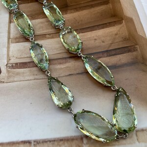May include: A silver chain necklace with large, faceted, light green gemstone pendants. The necklace is made of a silver chain with a lobster clasp.