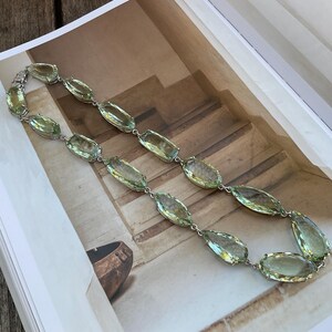 May include: A long necklace made of faceted, light green gemstones. The necklace is made of silver and has a simple design.