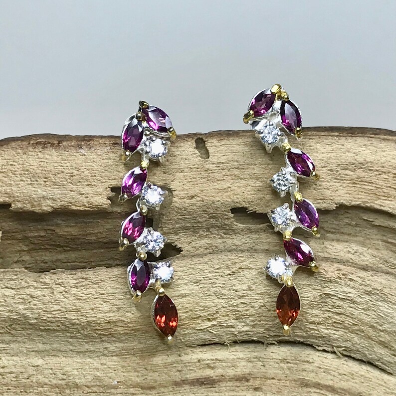 Puede incluir: Un par de pendientes de plata con un dise&ntilde;o en cascada de piedras de forma marquesa de color morado y rojo y piedras redondas transparentes.