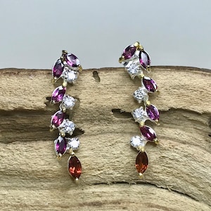 Puede incluir: Un par de pendientes de plata con una cascada de piedras preciosas en forma de marquesa de color morado y rojo y piedras redondas transparentes.