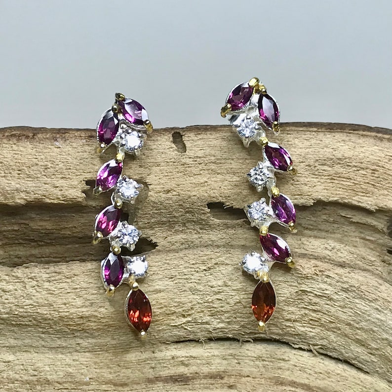 Puede incluir: Un par de pendientes de plata con una cascada de piedras preciosas en forma de marquesa de color morado y rojo y piedras redondas transparentes.