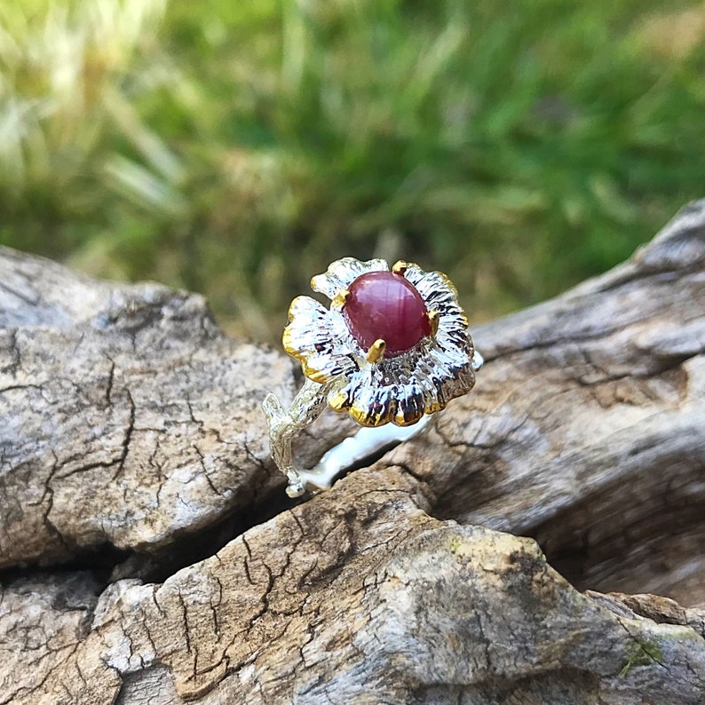 May include: A silver ring with a gold flower design and a red gemstone in the center.