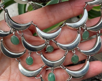 May include: Silver necklace with a crescent moon design and green gemstone accents.