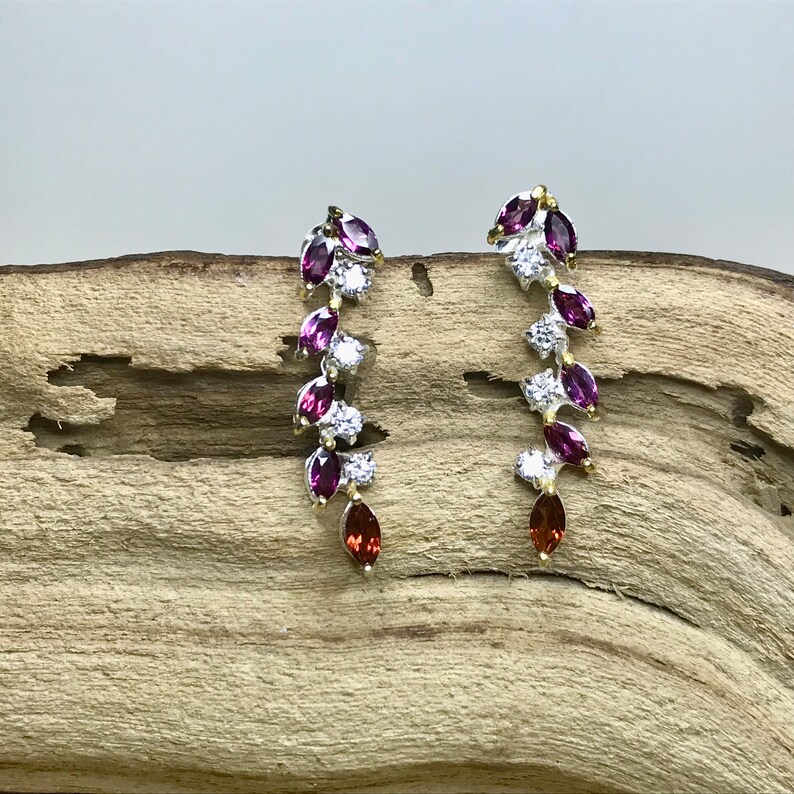 Puede incluir: Un par de pendientes colgantes de plata con una cascada de piedras preciosas p&uacute;rpuras y rojas y brillantes transparentes.