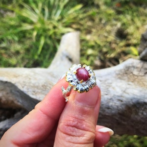 May include: A silver ring with a gold flower design and a pink star ruby gemstone.