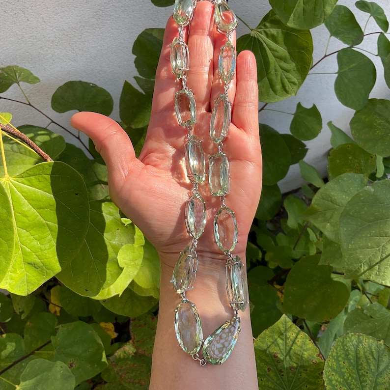 May include: A silver chain necklace with large, faceted, light green gemstone beads. The necklace is displayed on a hand.