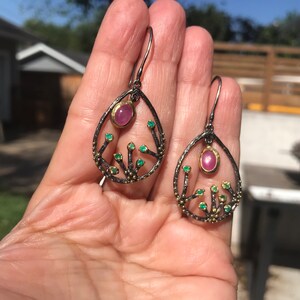 May include: A pair of dangle earrings with a delicate, tree-like design. The earrings are made of oxidized silver and feature a pink gemstone and smaller green gemstones.