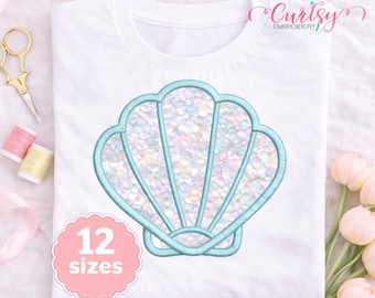 May include: A white t-shirt featuring a central embroidered seashell design with a light blue outline and a shimmering, iridescent sequin-like fill. A pink scalloped badge on the lower left displays the text 12 sizes in white.