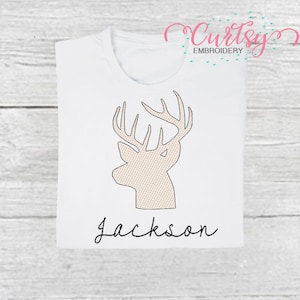 May include: White t-shirt with a beige embroidered deer head and the name "Jackson" in black script.