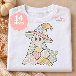 Op de afbeelding: Een wit t-shirt met een geborduurde patchwork geest die een heksenhoed draagt. De geest is samengesteld uit verschillende pastelkleurige stoffen segmenten met kruissteekpatronen. Een roze geschulpte badge toont de tekst 14 sizes.