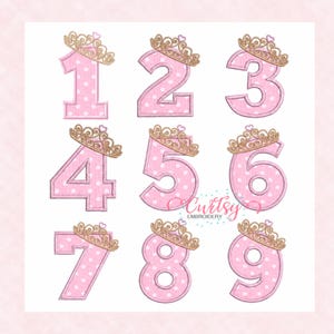May include: A set of pink numbers from one to nine, each featuring a white polka dot pattern and a gold-colored crown with a small heart on top. The text Curtsy EMBROIDERY is visible in the center. Each number has a stitched border.