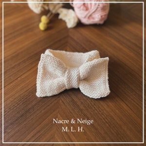 Pode incluir: Uma gravata borboleta de malha branca com uma superfície texturizada. A gravata borboleta está sobre uma superfície de madeira. Nacre & Neige M. L. H.