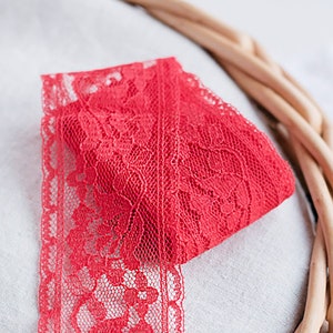 May include: Red lace trim with a floral pattern. The lace is folded in half and placed on a woven basket.