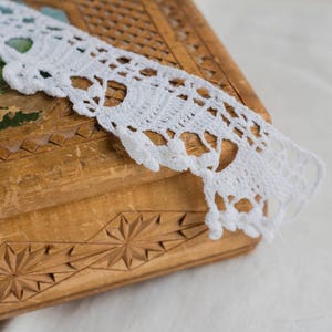 Może przedstawiać: Drewniana skrzynia z misternymi rzeźbami i białą koronkową lamówką wykonaną na szydełku.