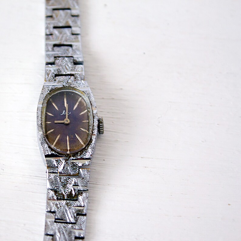May include: A silver wristwatch with a dark brown face and a patterned metal band.