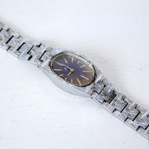 May include: A silver wristwatch with a dark blue face and a silver metal band. The watch has a simple design with a round face and a silver metal band.