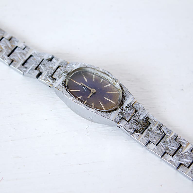 May include: A silver wristwatch with a dark blue face and a silver metal band. The watch has a simple design with a round face and a silver metal band.