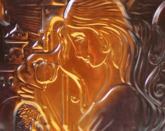 May include: A brown ceramic tile with a raised relief design of a woman with long hair. The woman is holding a flower in her hand and is looking to the side. The tile has a glossy finish.