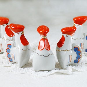 Puede incluir: Conjunto de cinco saleros y pimenteros de porcelana en forma de gallo. Los gallos son blancos con crestas y barbillas rojas, plumas de cola azules y blancas y detalles dorados.