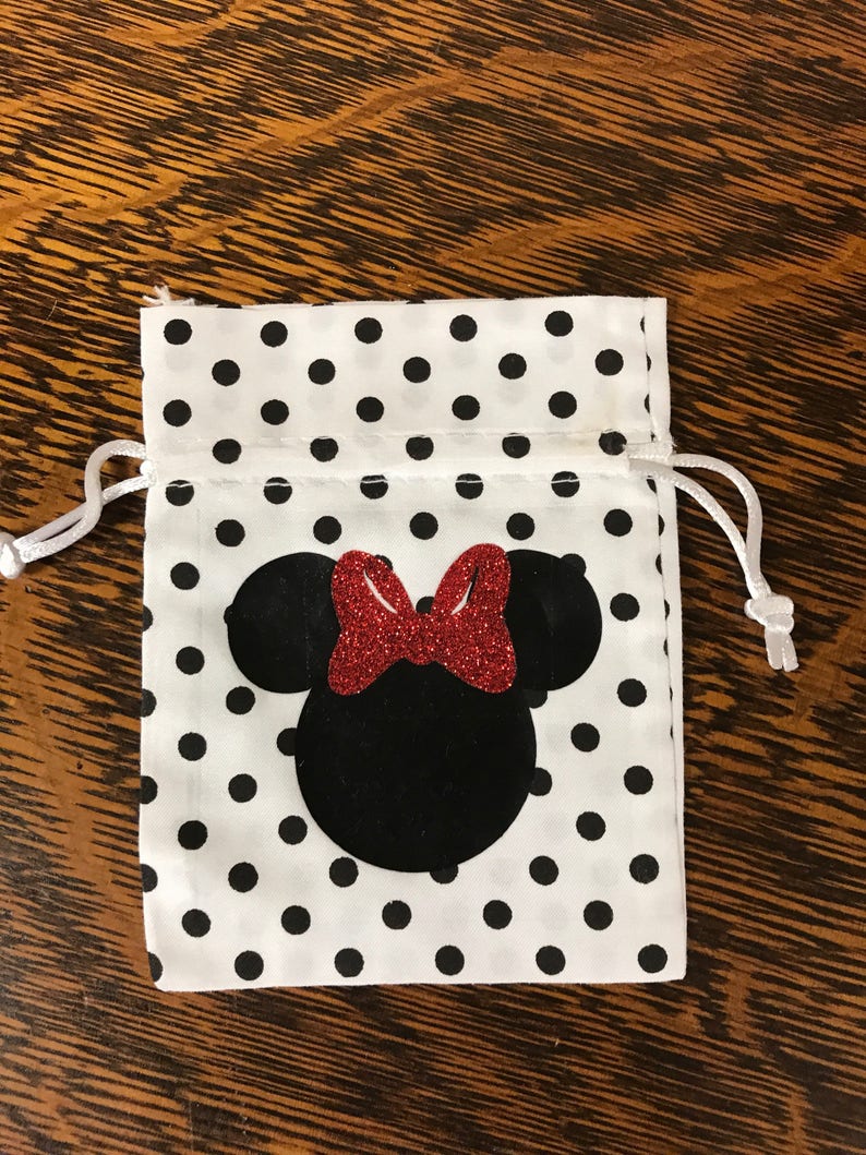 Puede incluir: Una bolsa de cord&oacute;n blanca con lunares negros y una silueta de Minnie Mouse negra y roja.