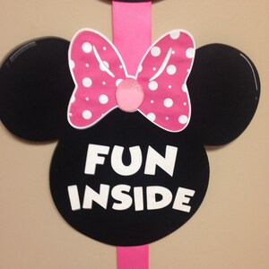 May include: Black and white Minnie Mouse ears with a pink bow and white polka dots. The ears have the text "FUN INSIDE" written in white.